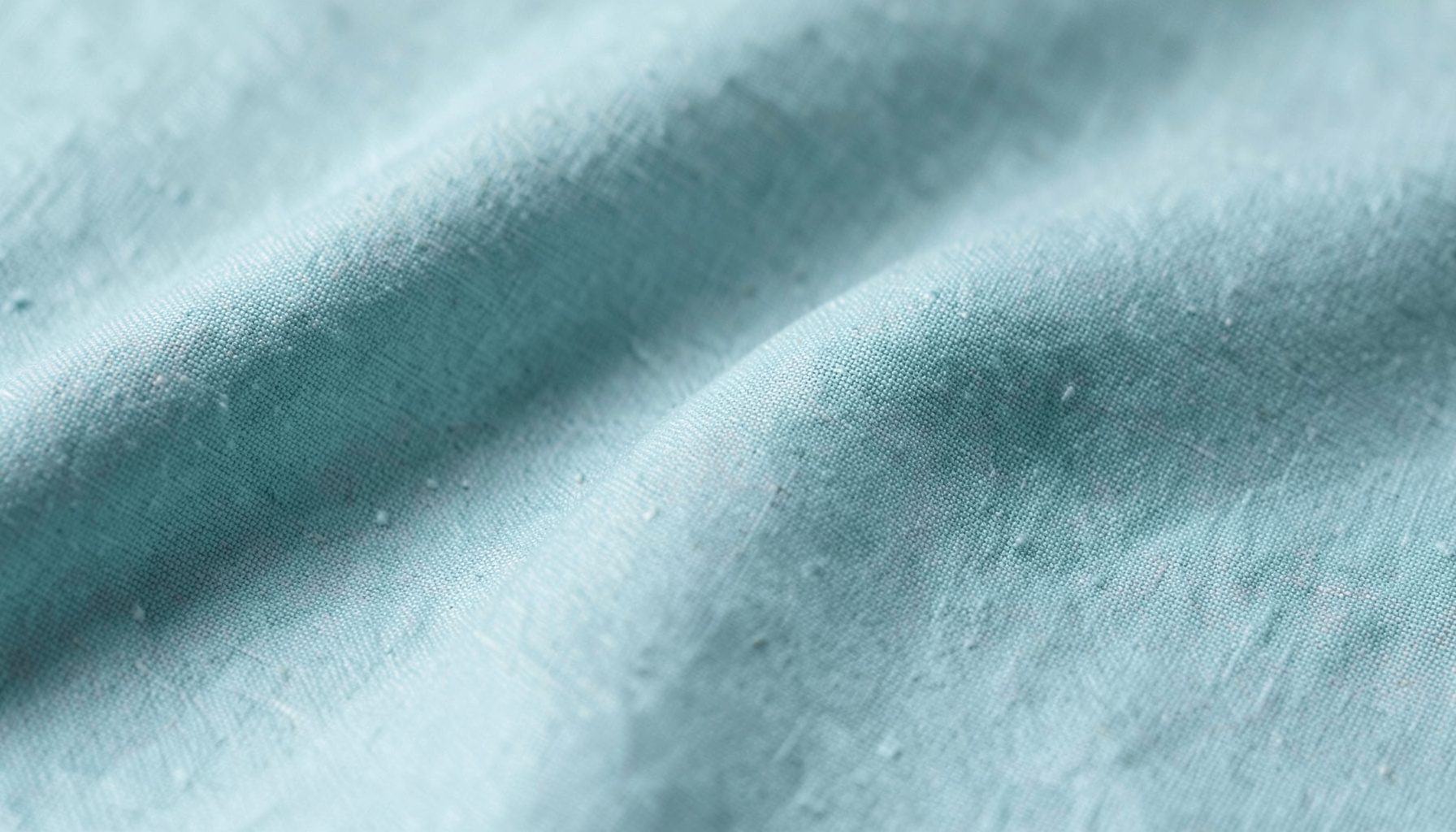 Soft sage linen fabric folds under cool studio light in a flat lay close-up
